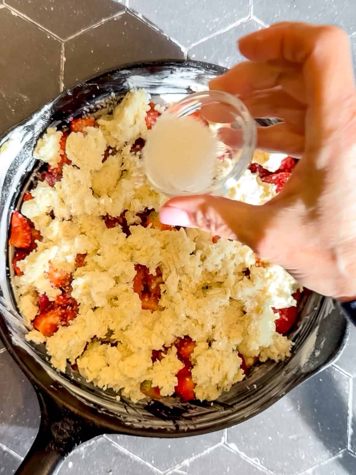 Sprinkling coarse sugar on top of biscuit topping before putting strawberry cobbler into the oven.