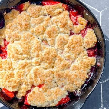 Cast-iron pan containing a strawberry biscuit cobbler on a black tile counter.