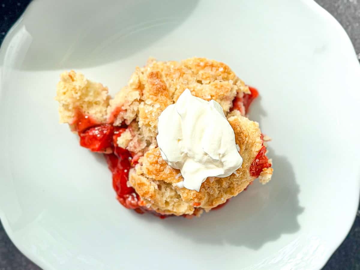 Strawberry cobbler on a white plate on a black tile counter.