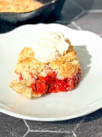 Strawberry cobbler on a white plate on a black tile counter.
