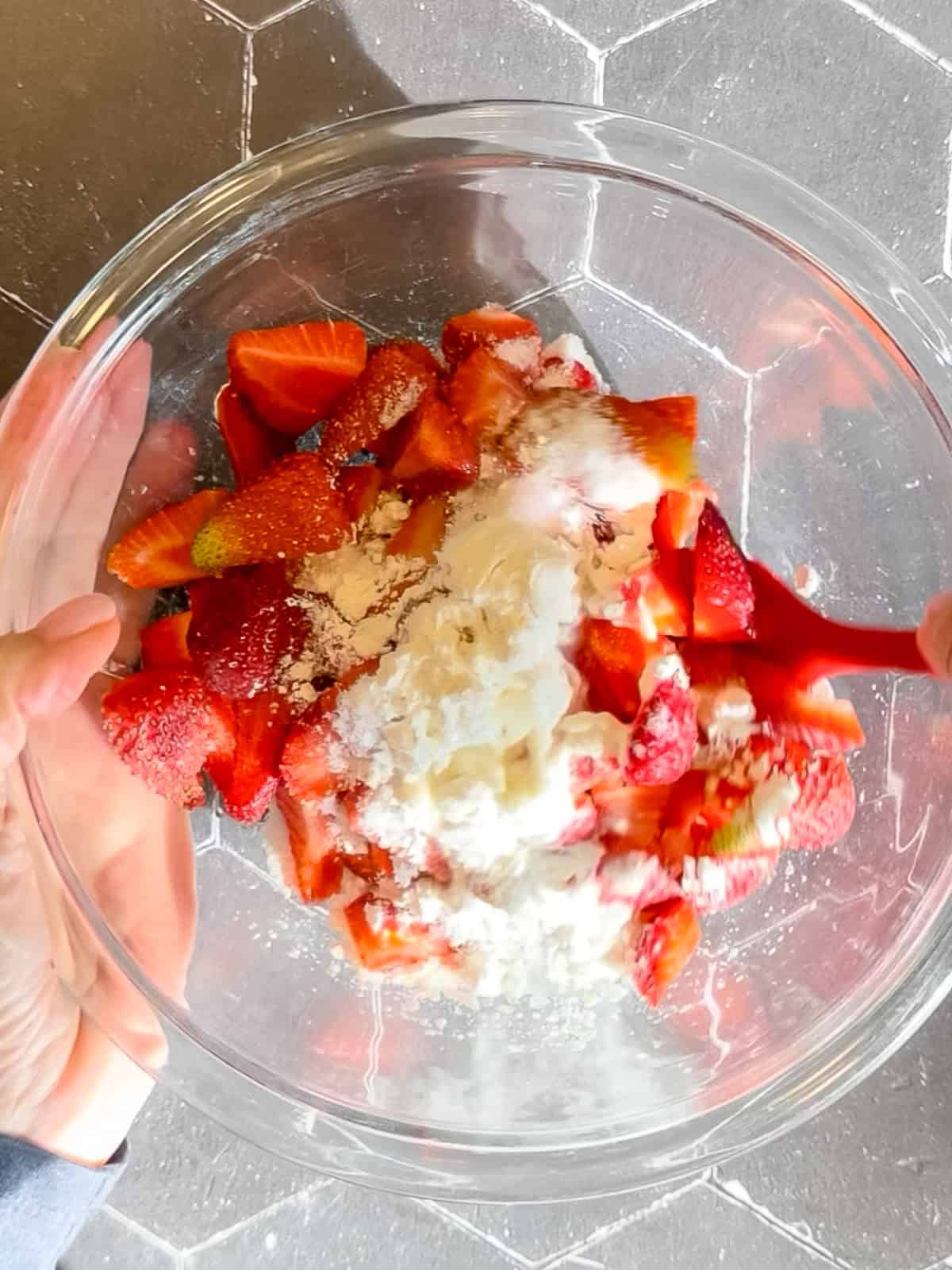 Mixing cut strawberries, sugar, cornstarch, and lemon juice in a glass bowl.