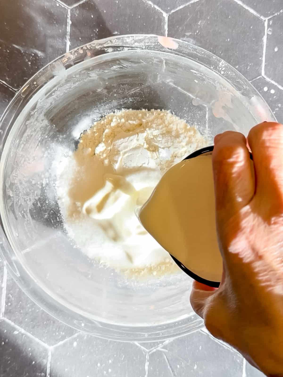 Adding heavy cream to sugar and self rising flour in a glass bowl.