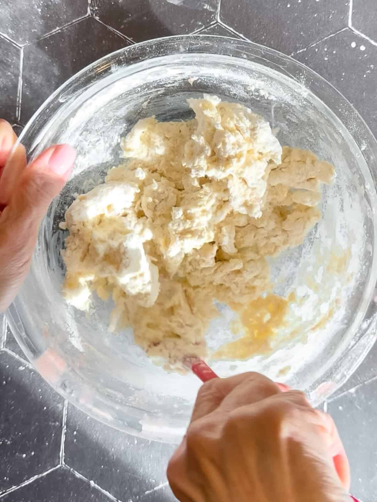 Mixing biscuit dough in a glass bowl on a black tile background.