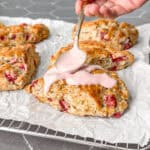 Using a spoon to add a strawberry glaze on top of baked strawberry and rosemary scones.
