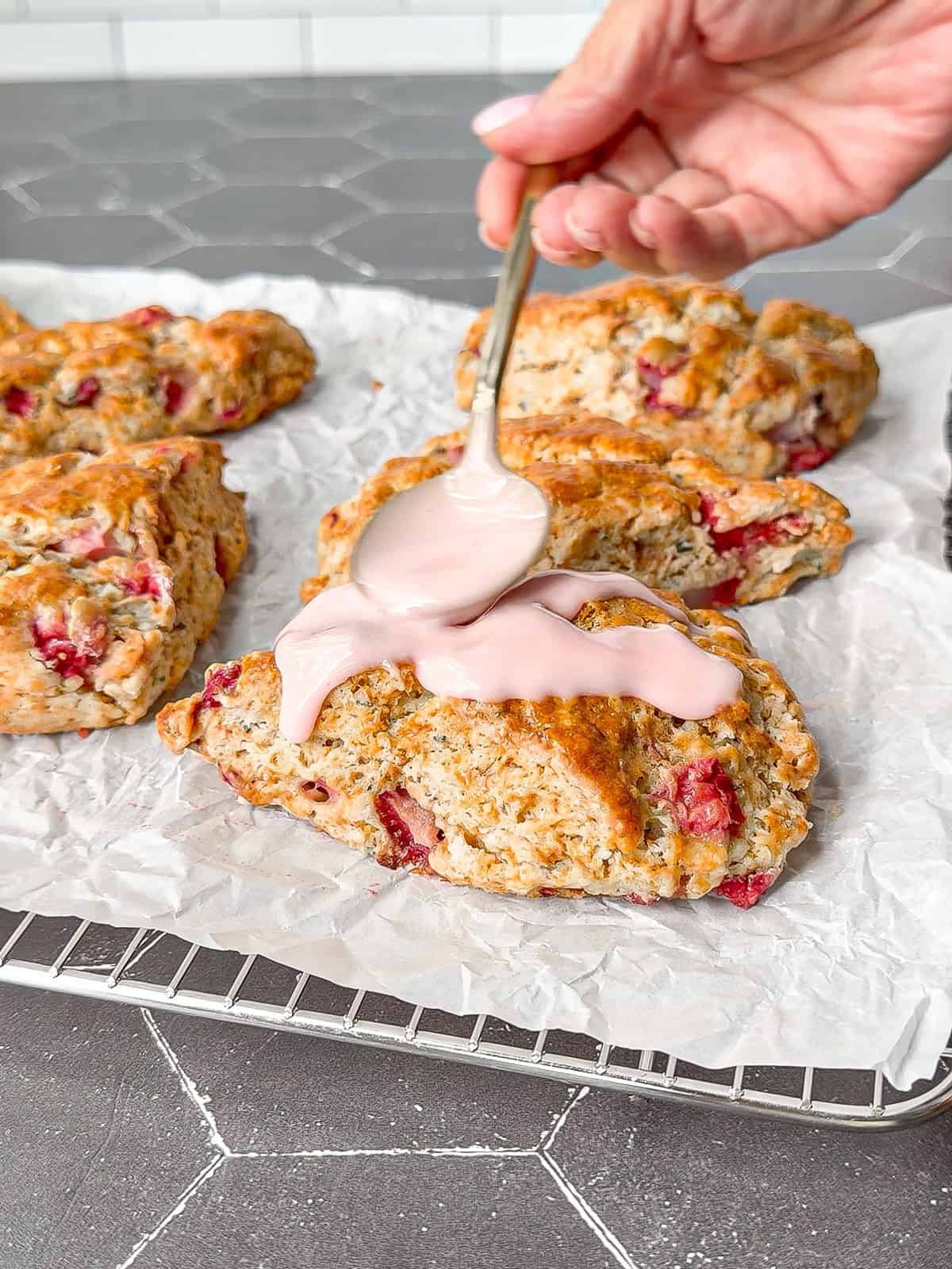 Using a spoon to add a strawberry glaze on top of baked strawberry and rosemary scones.