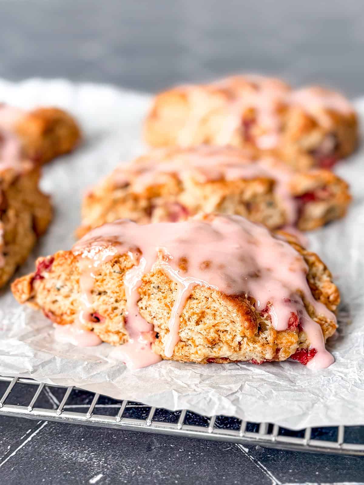 Glazed strawberry scones on a parchment paper covered wire rack.