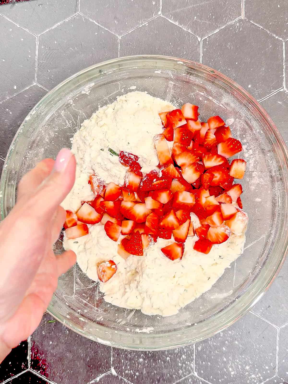 Adding diced strawberries to dry ingredients to make strawberry scones.