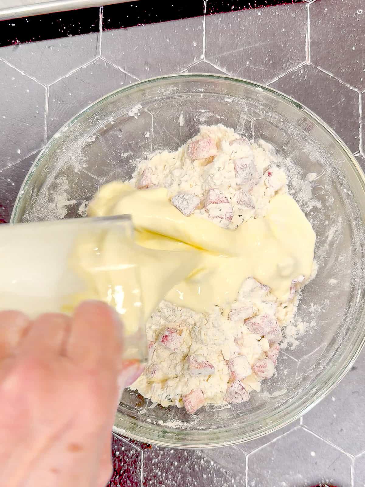 Adding heavy cream that has been whisked with one egg and a splash of vanilla over dry ingredients to make strawberries scones.
