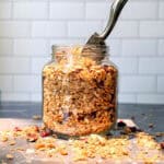 Jar of baked granola on a Black counter.