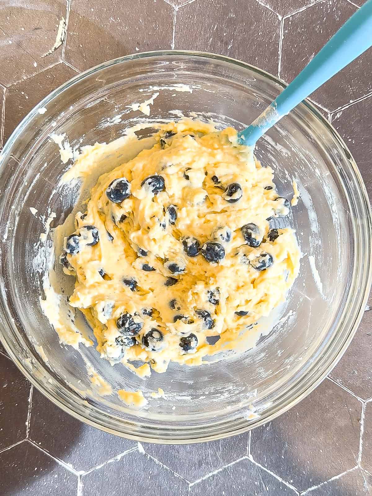 Blueberry muffin batter in a glass bowl with a blue spatula.