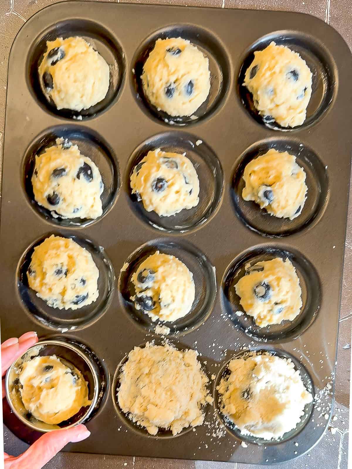 Adding crumb topping to unbaked blueberry muffin tops.