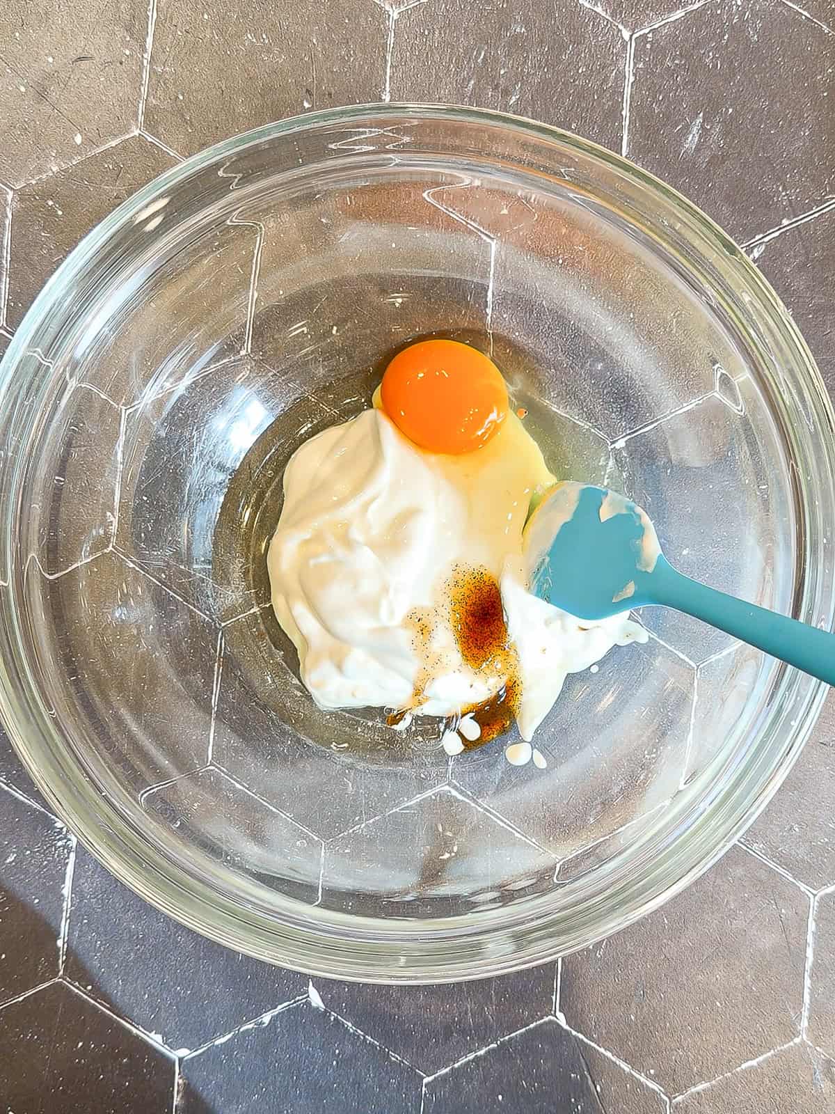 Greek yogurt, egg, and vanilla with a blue spatula in a glass bowl.
