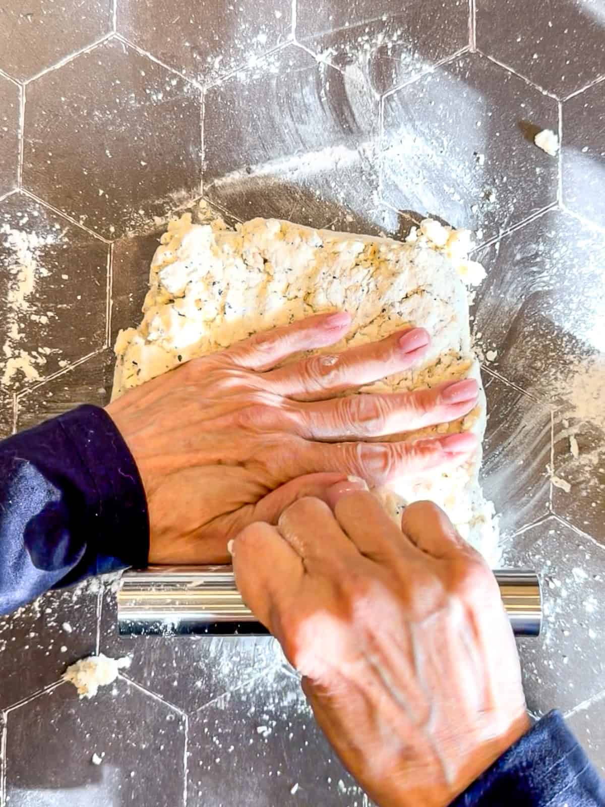 Using a bench scraper to shape biscuit dough into a square on a black background.