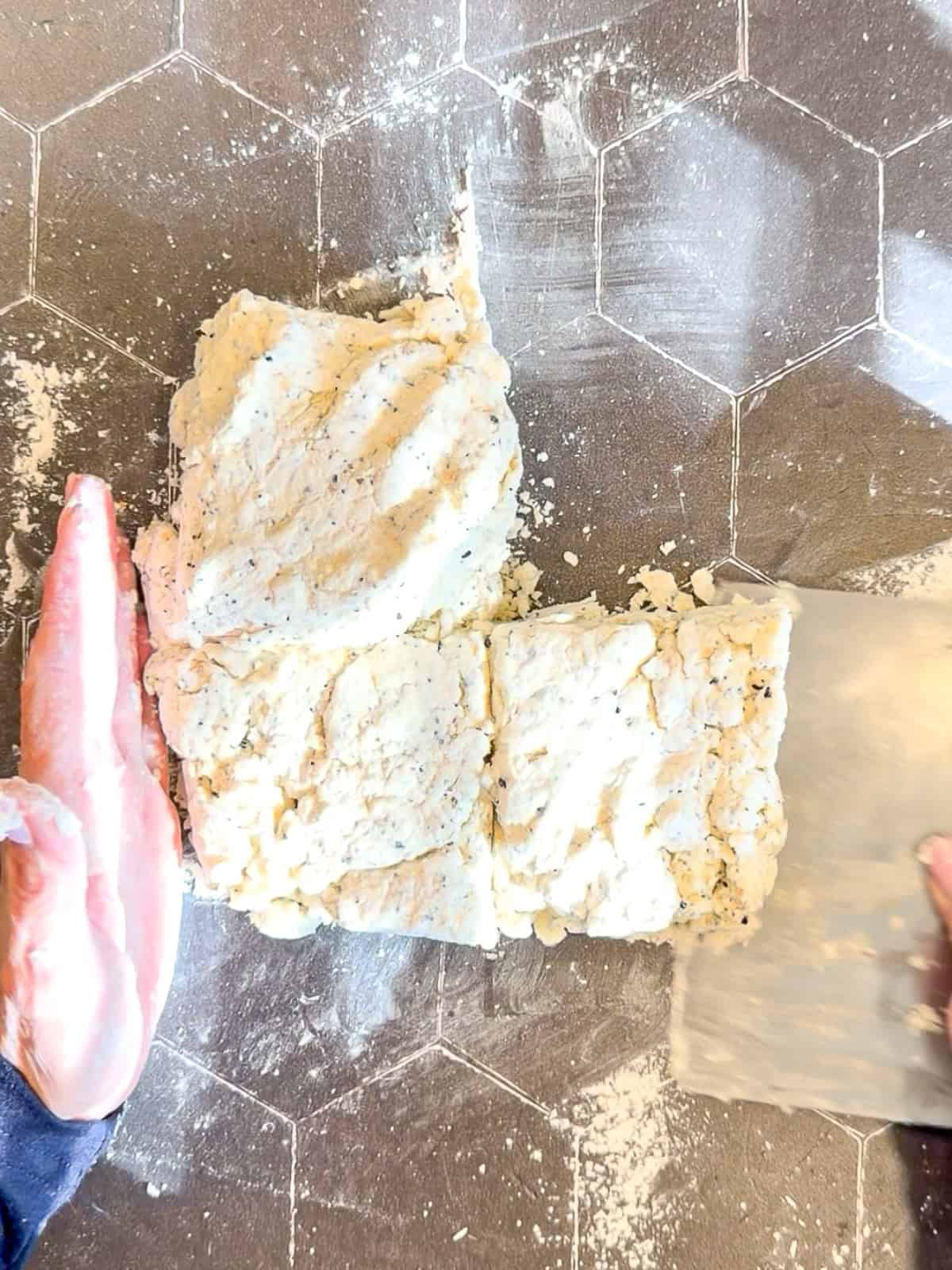 Stacking pieces of cream cheese biscuit dough on top of each other with a bench scraper.