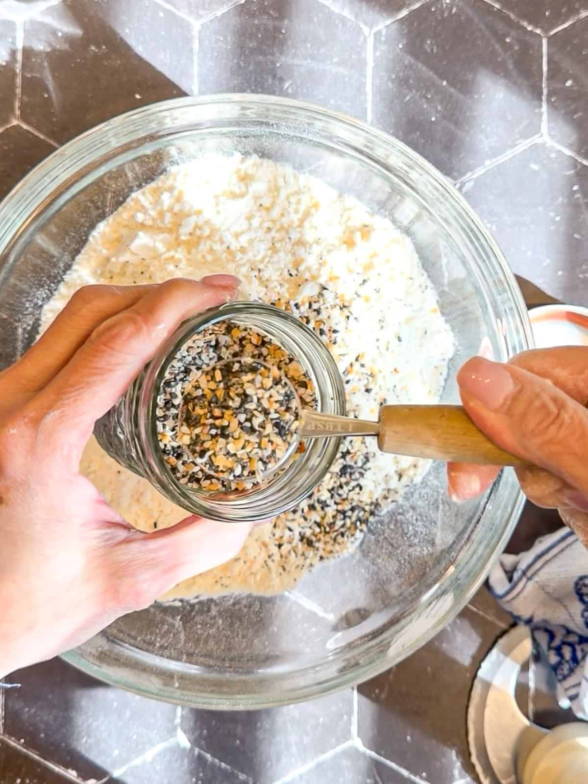 Adding everything bagel seasoning to flour and butter mixture in a glass bowl.