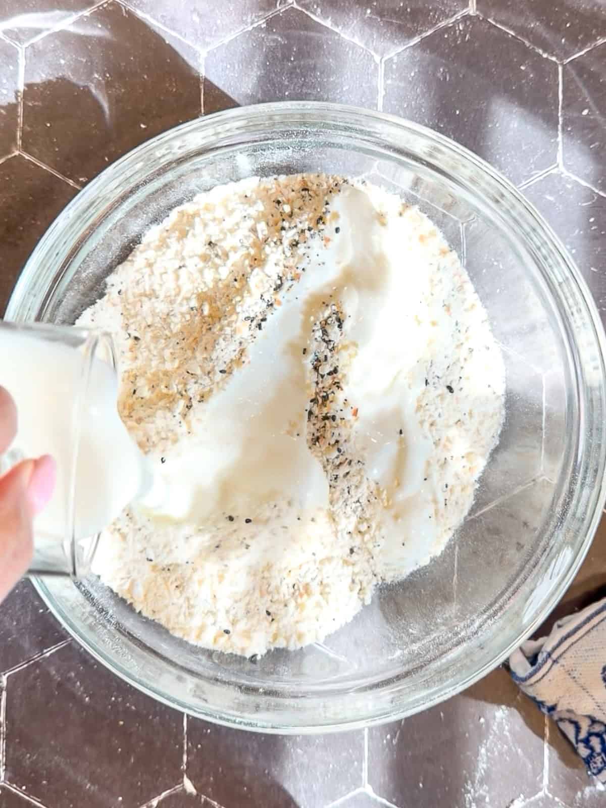 Pouring buttermilk into flour and everything seasoning mixture in a glass bowl.