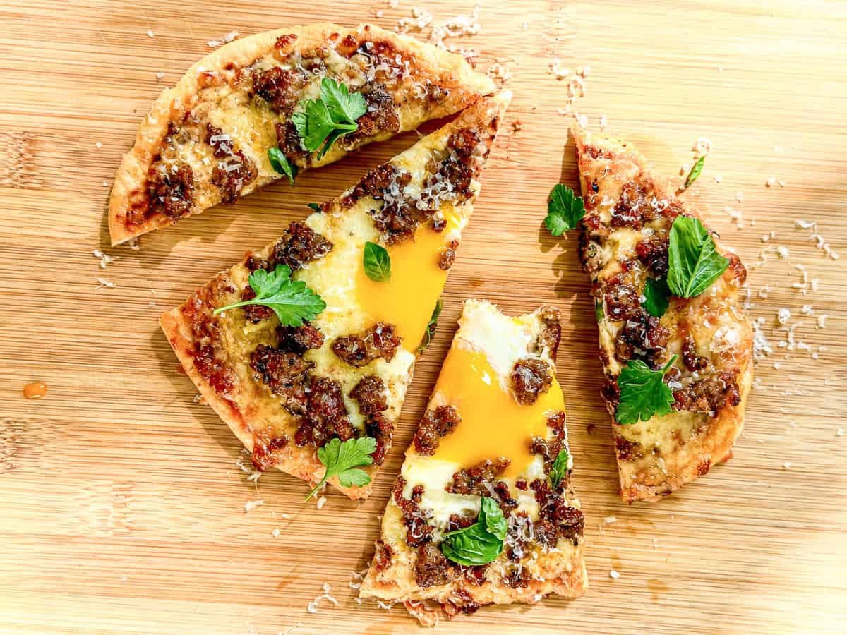 Sliced flatbread breakfast pizza on a wooden cutting board.
