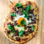 Flatbread breakfast pizza on a wooden cutting board.