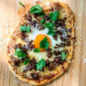Flatbread breakfast pizza on a wooden cutting board.