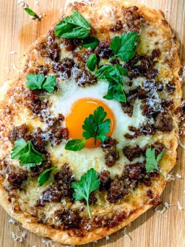 Flatbread breakfast pizza on a wooden cutting board.