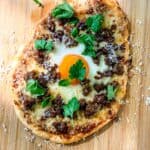 Flatbread breakfast pizza on a wooden cutting board.