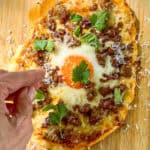 Adding Parmesan cheese and fresh herbs to flatbread breakfast pizza.