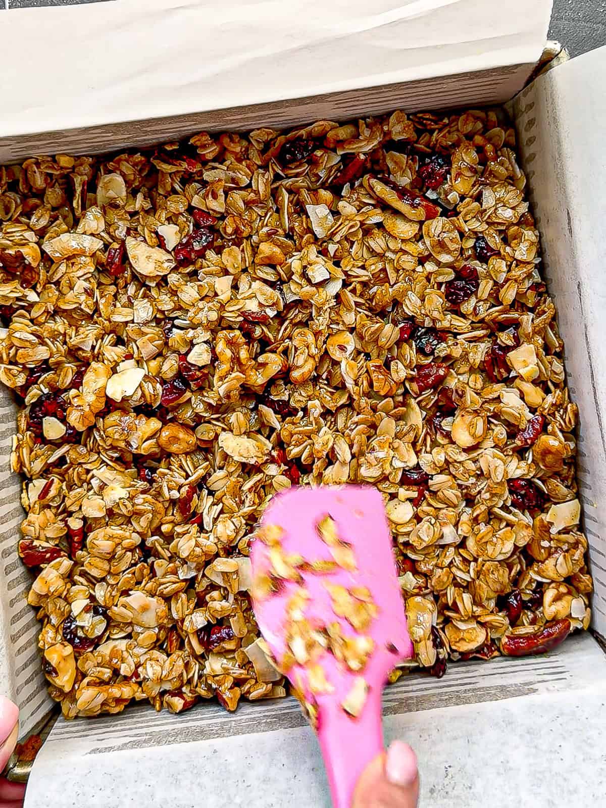 Using a silicone spatula to press granola into a pan.