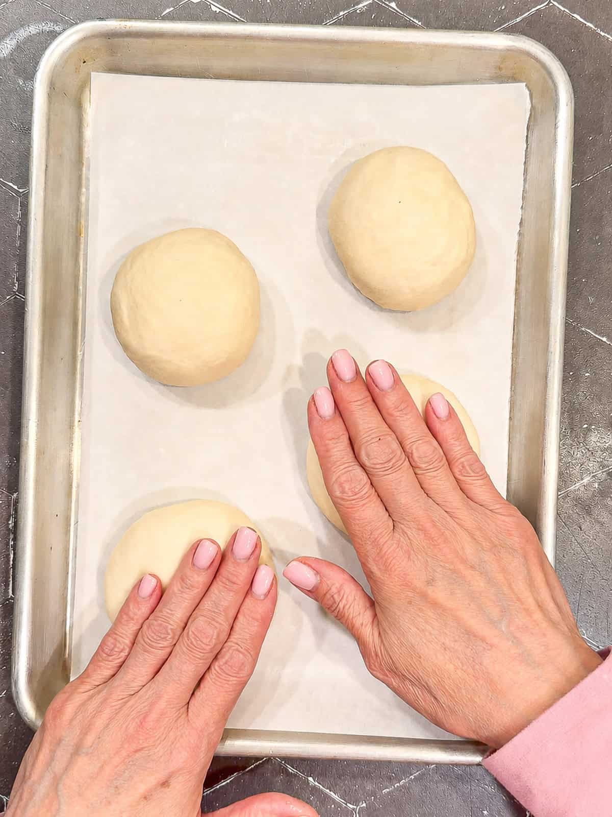 Pressing the tops of unbaked hamburger buns.