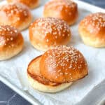 Sesame seed hamburger buns on parchment paper, one of them toasted.