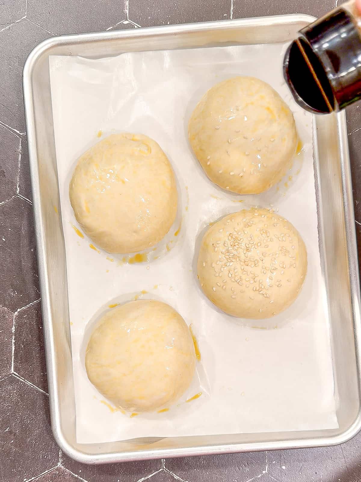 Sprinkling sesame seeds on unbaked hamburger buns.