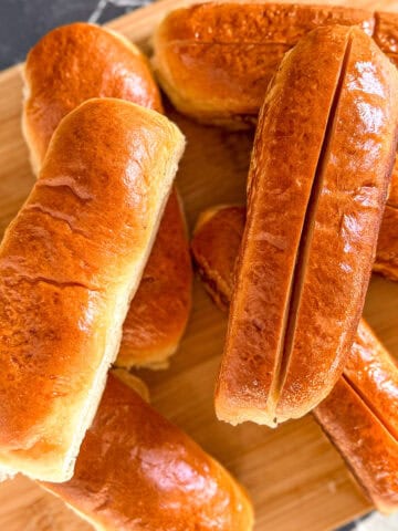 Hot dog buns on a wooden cutting board.