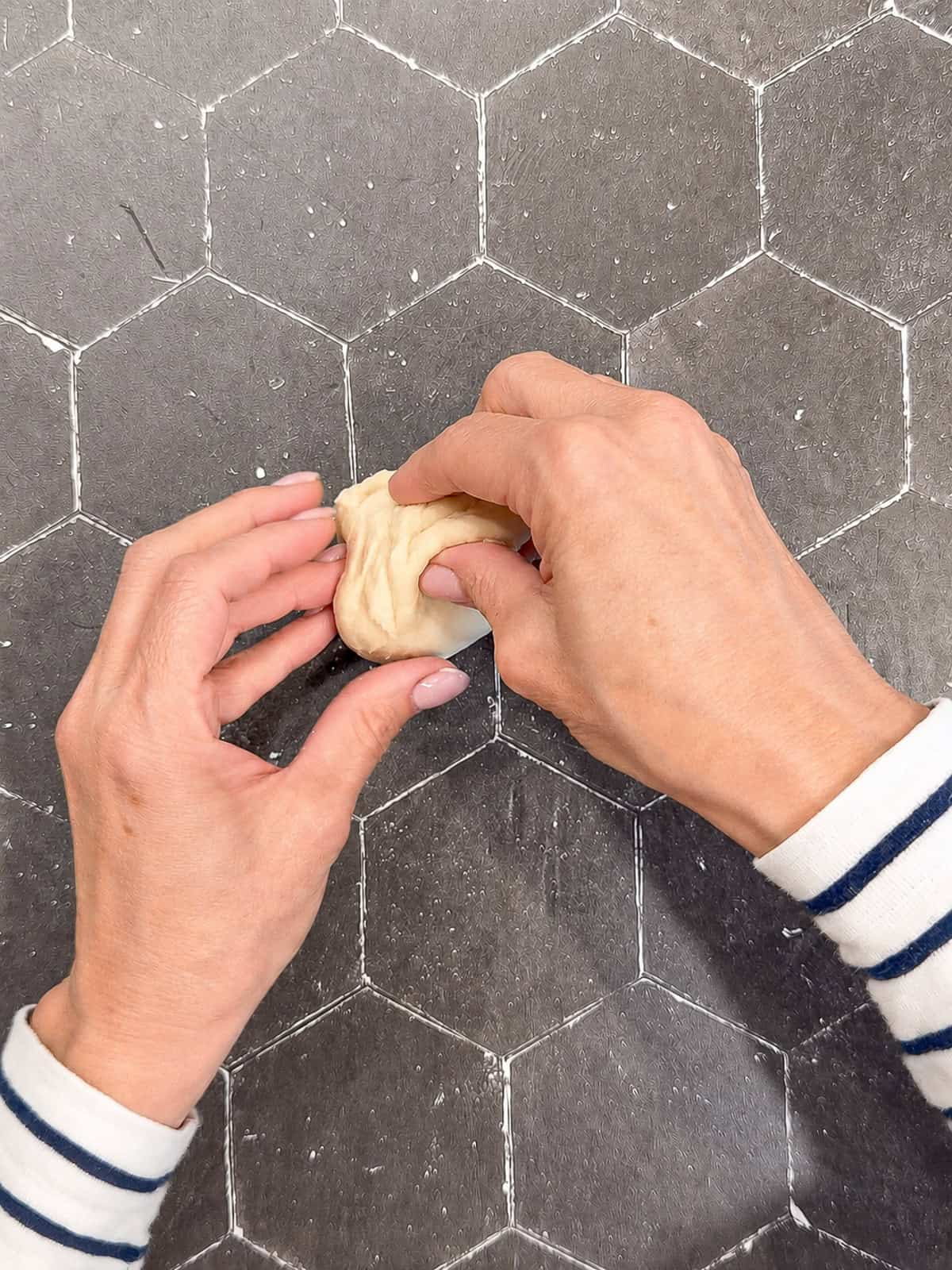 Pinching a ball of dough closed on a black counter.