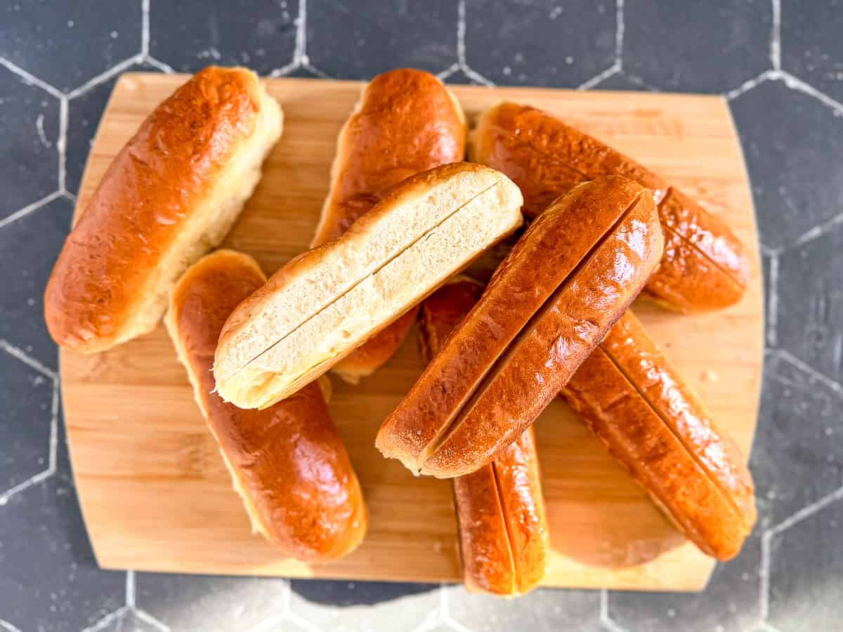 Hot dog buns on a wooden cutting board.