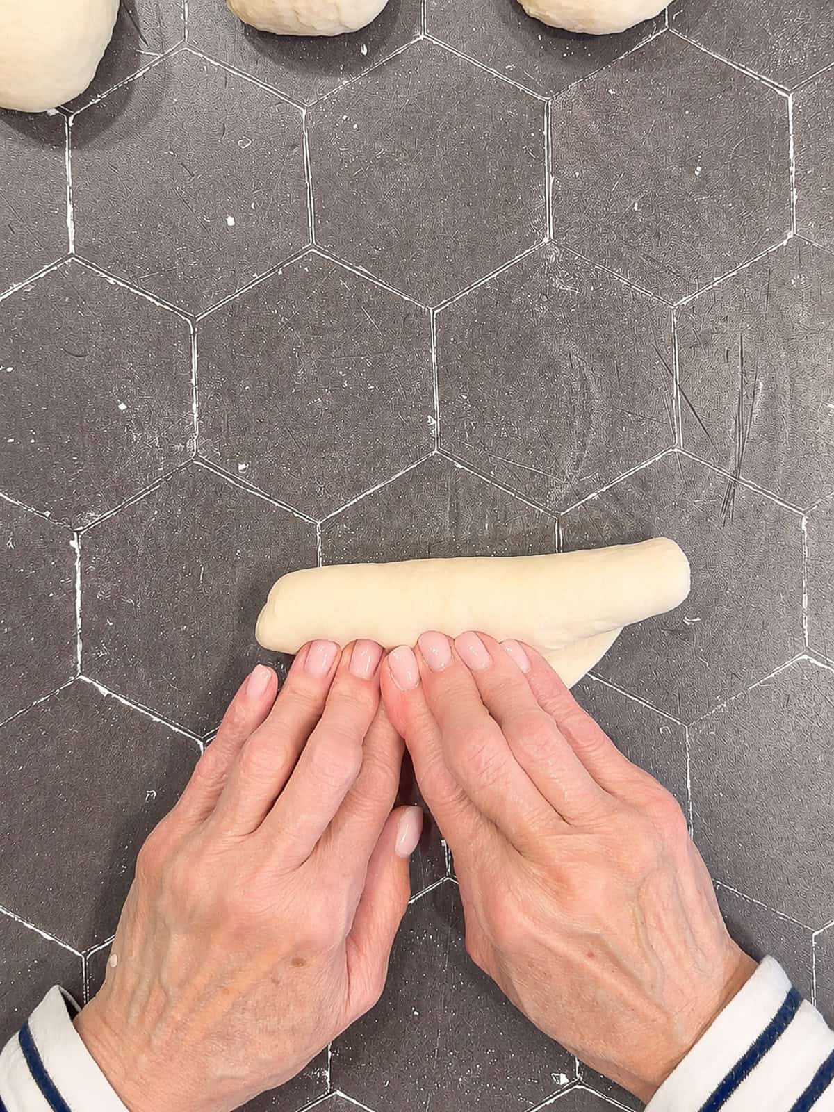 Shaping hot dog bun dough on a black counter.