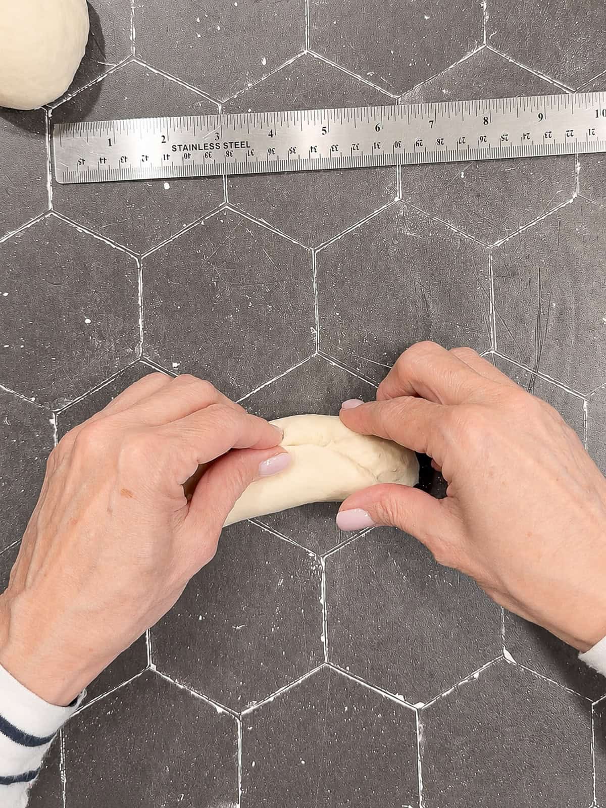 Pinching a seam of dough closed on a black counter with a ruler nearby.