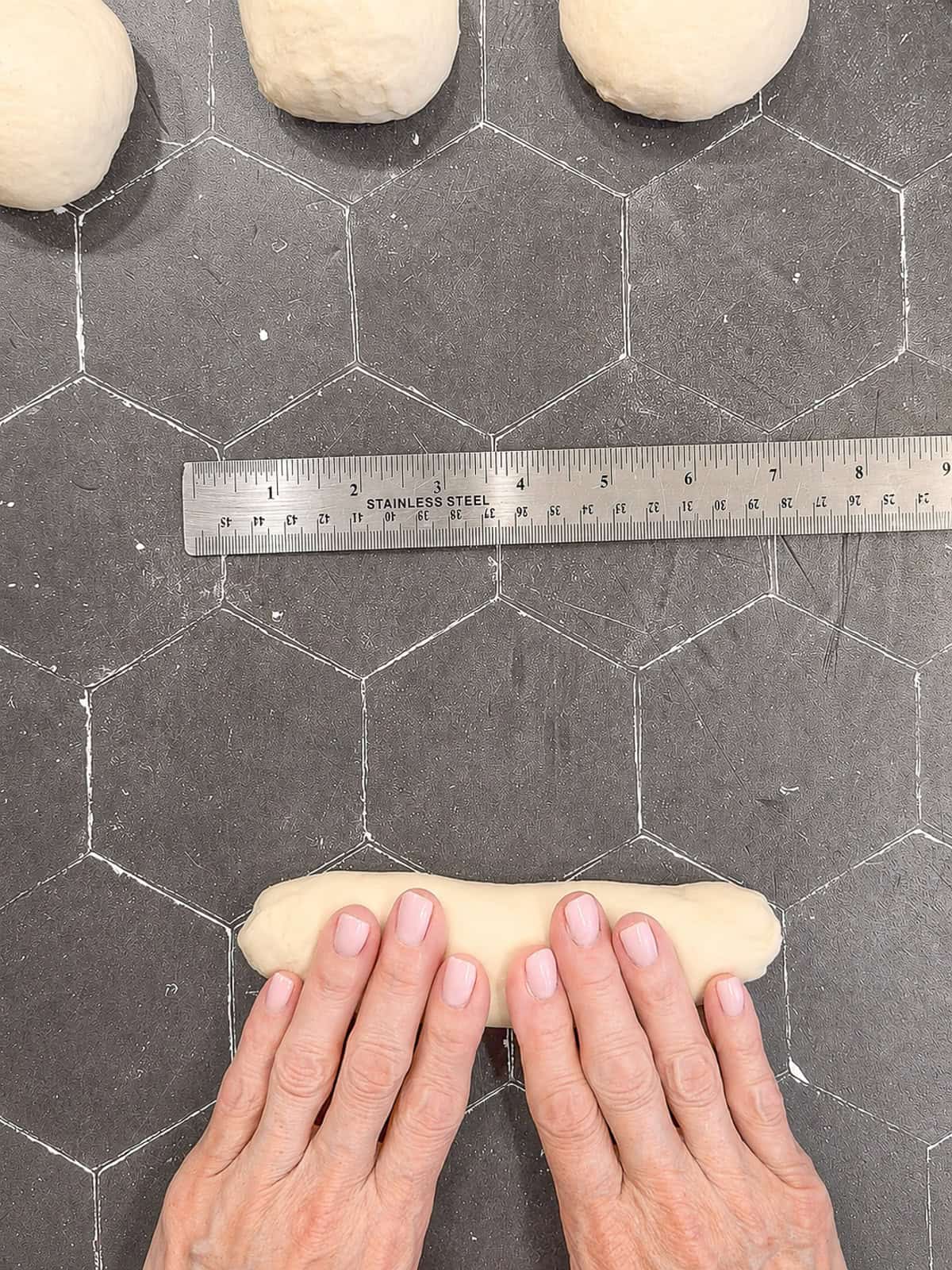 Rolling hot dog bun dough on a counter with a ruler nearby.