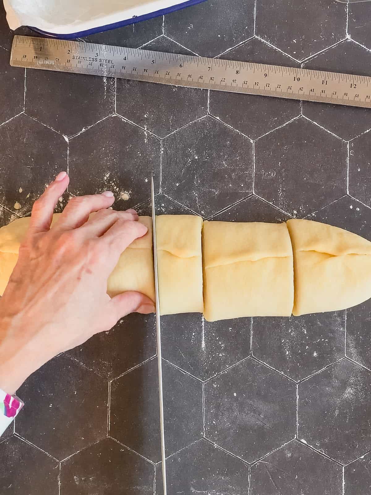 Using a knife to slice a log of brioche dough into pieces.