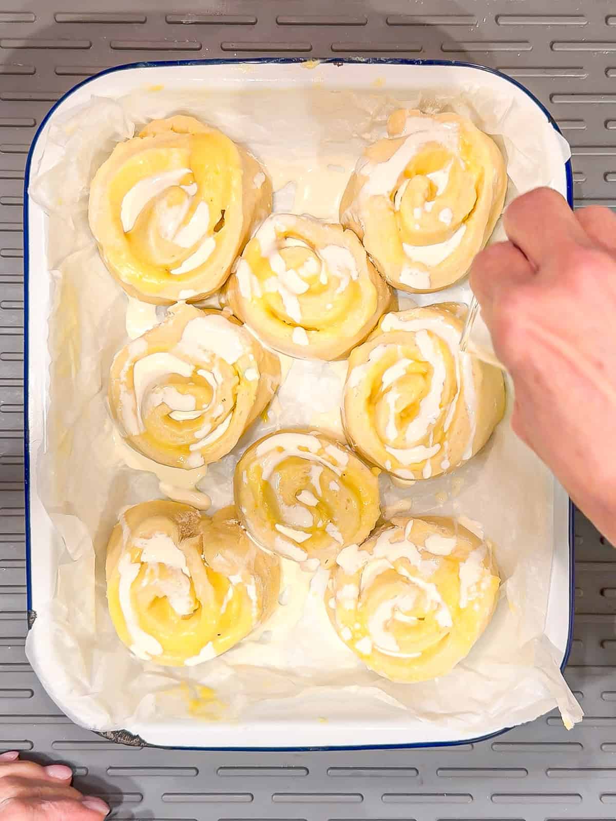 Drizzling heavy cream on top of and round lemon rolls before baking.