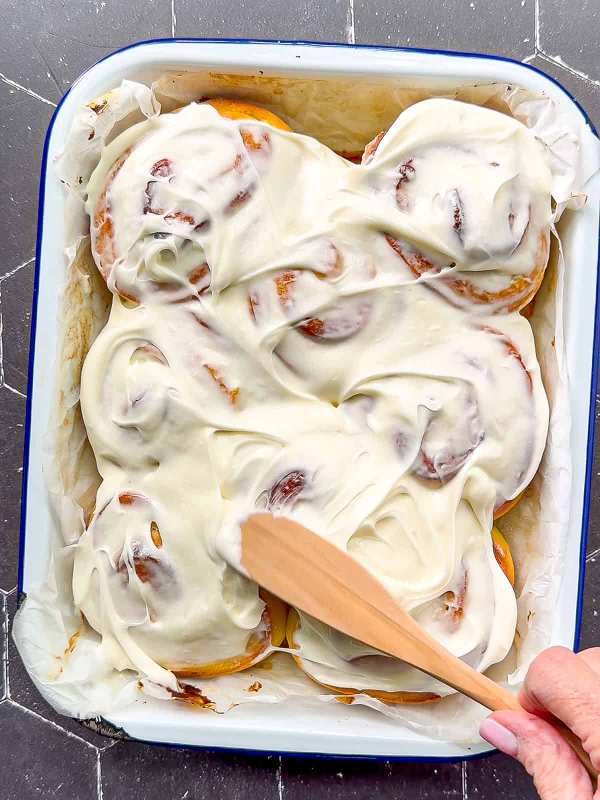 Swirling cream cheese frosting on top of lemon rolls.