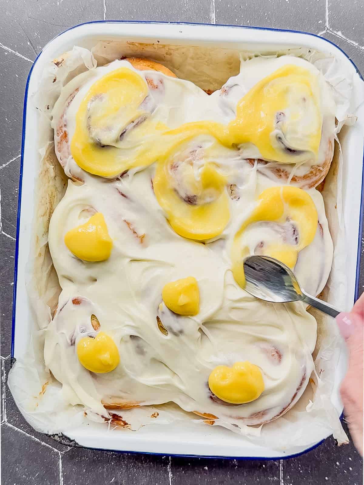 Swirling lemon curd into frosting on top of lemon rolls.