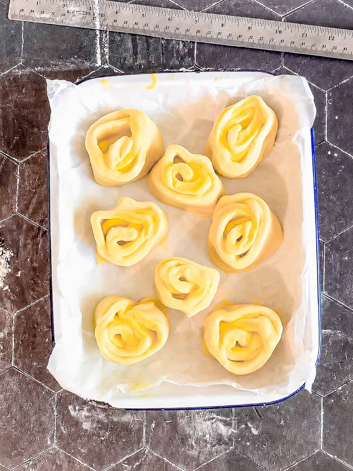 Unbaked lemon rolls in a white pan before rising.