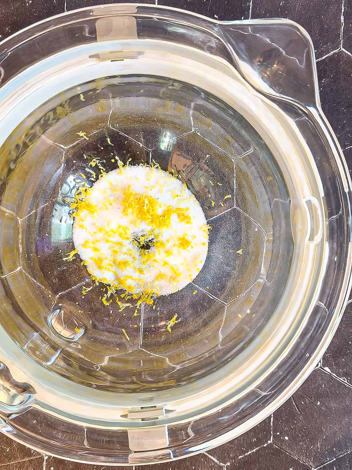 Granulated sugar and lemon zest in a glass stand mixer bowl.