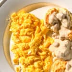 Creamy mascarpone eggs on a white plate with biscuits and gravy.