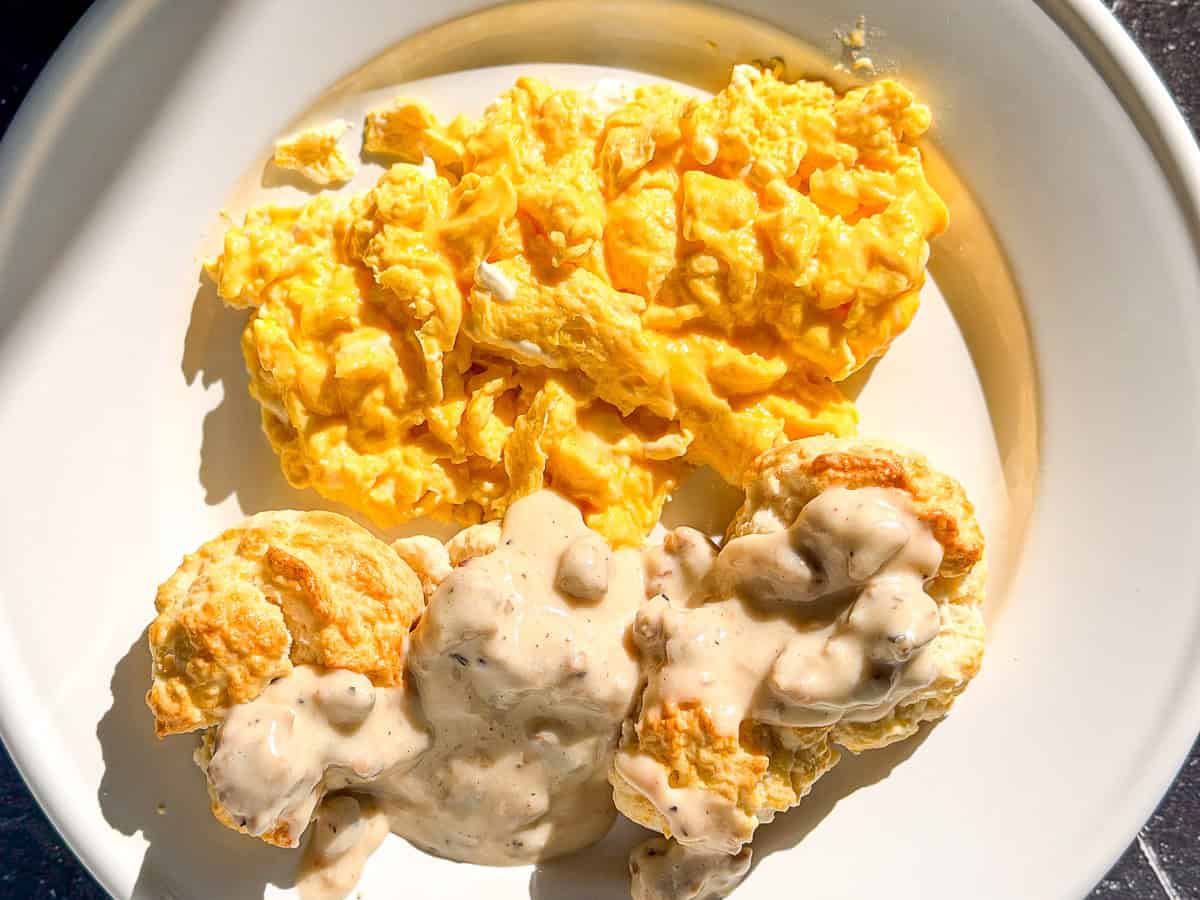 Creamy mascarpone eggs on a white plate with biscuits and gravy.