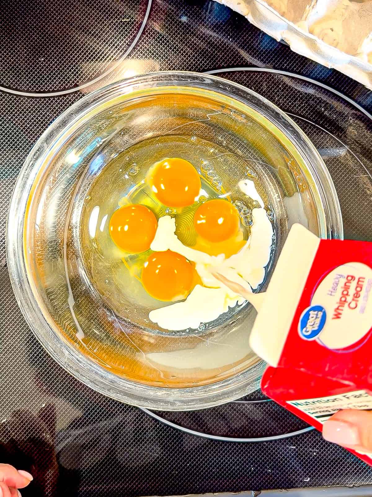 Pouring heavy cream into eggs in a glass bowl.