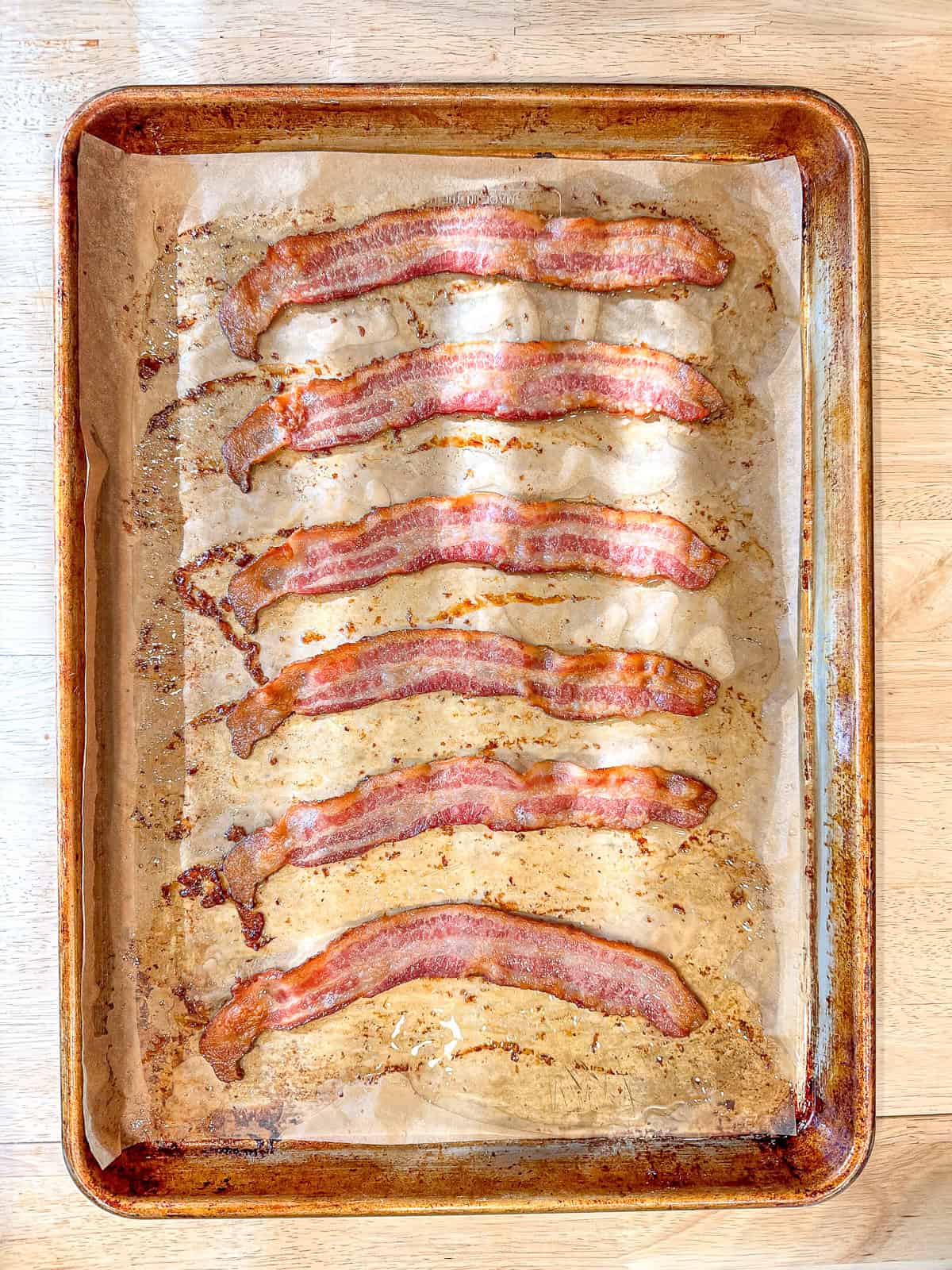 Cooked bacon strips on an parchment paper covered sheet pan.