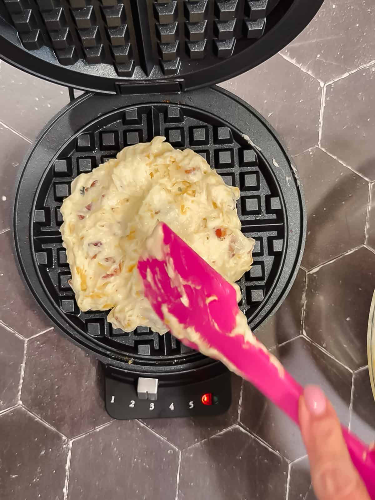 Spreading bacon cheddar waffle batter in a waffle maker.