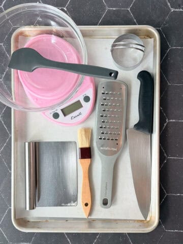 Biscuit baking tools on a sheet pan on a black tile background.