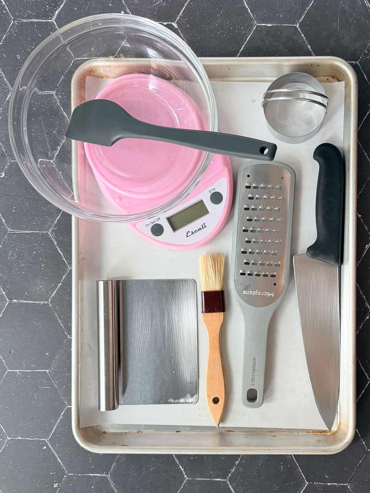 Biscuit baking tools on a sheet pan on a black tile background.