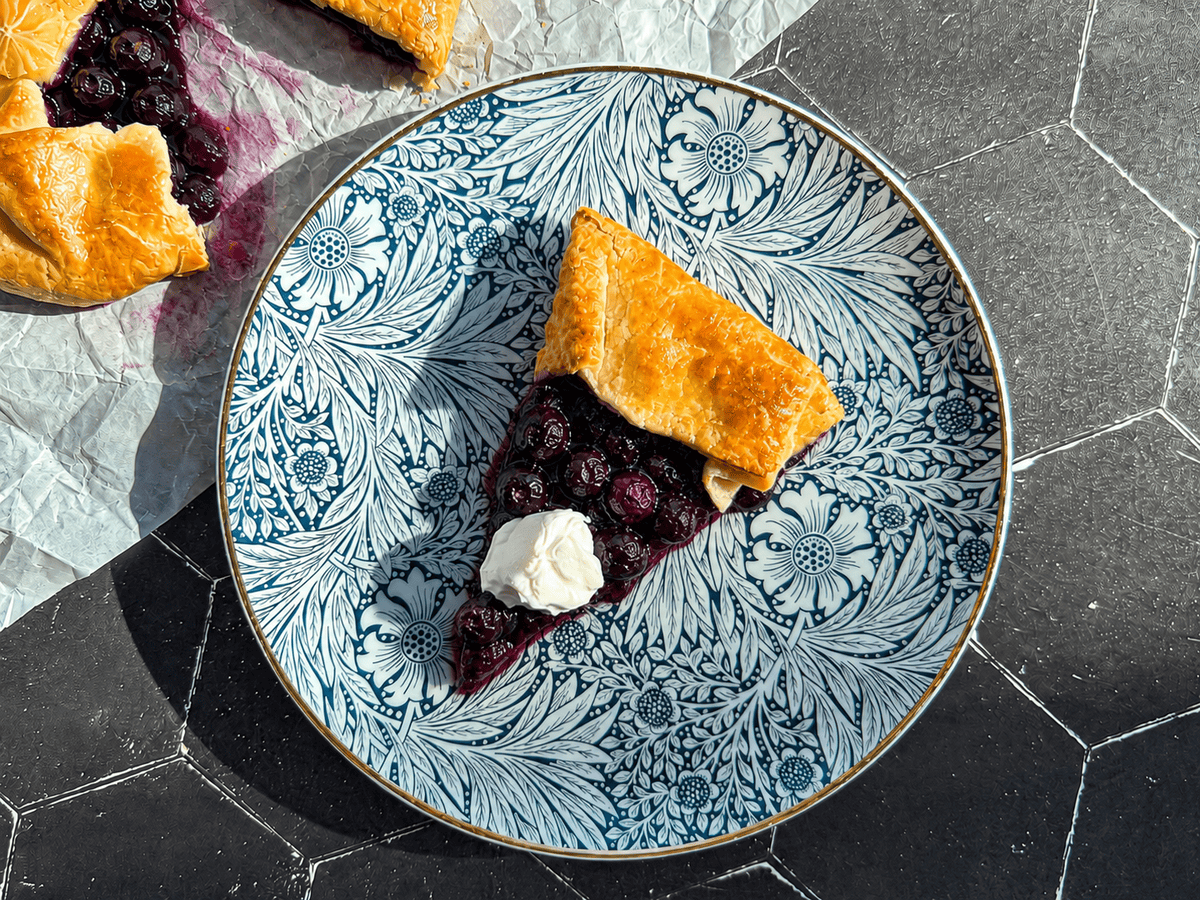 Slice of blueberry Galette on a blue floral plate on a black background.